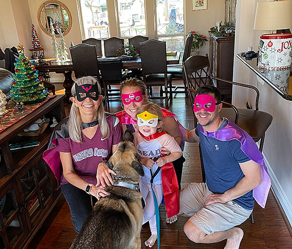 Photo - A young girl dressed as a superhero poses with three adults in similar costumes