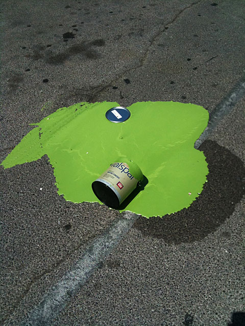 Photo of a can of green paint spilled in a parking lot