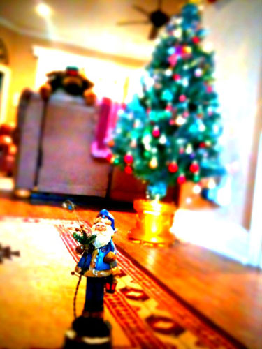 Photo of toy Santa against lit Christmas tree